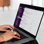 A woman types on a laptop using a messaging app in a modern office setting.